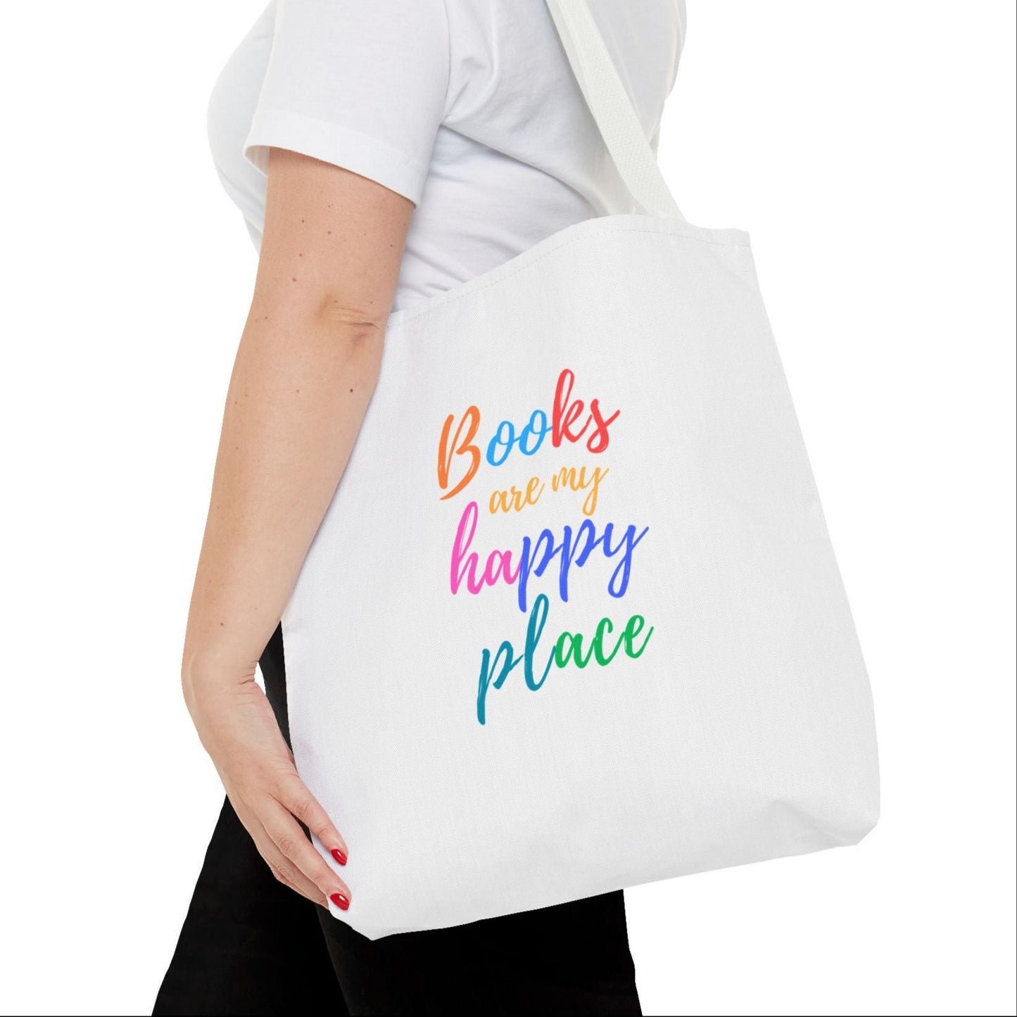 A person holding a white tote bag with the text 'Books are my happy place' printed in colorful letters.
