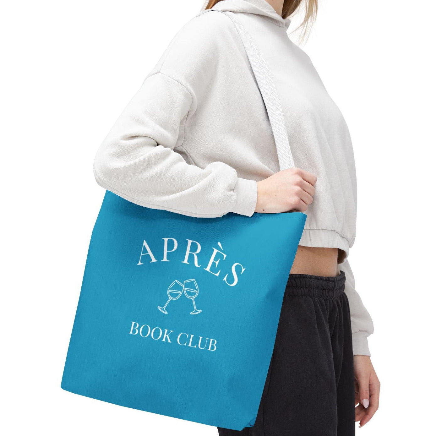 Person holding a blue tote bag with 'APRèS BOOK CLUB' text on a white background