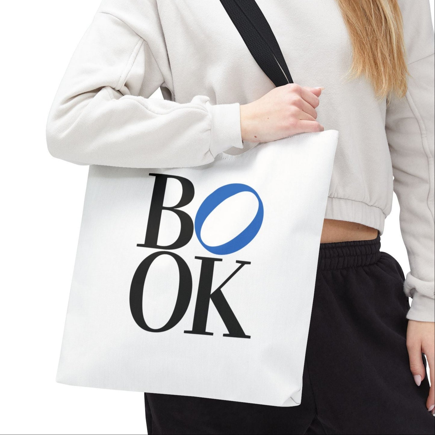 Person holding a white tote bag with 'BOOK' printed on it against a white background