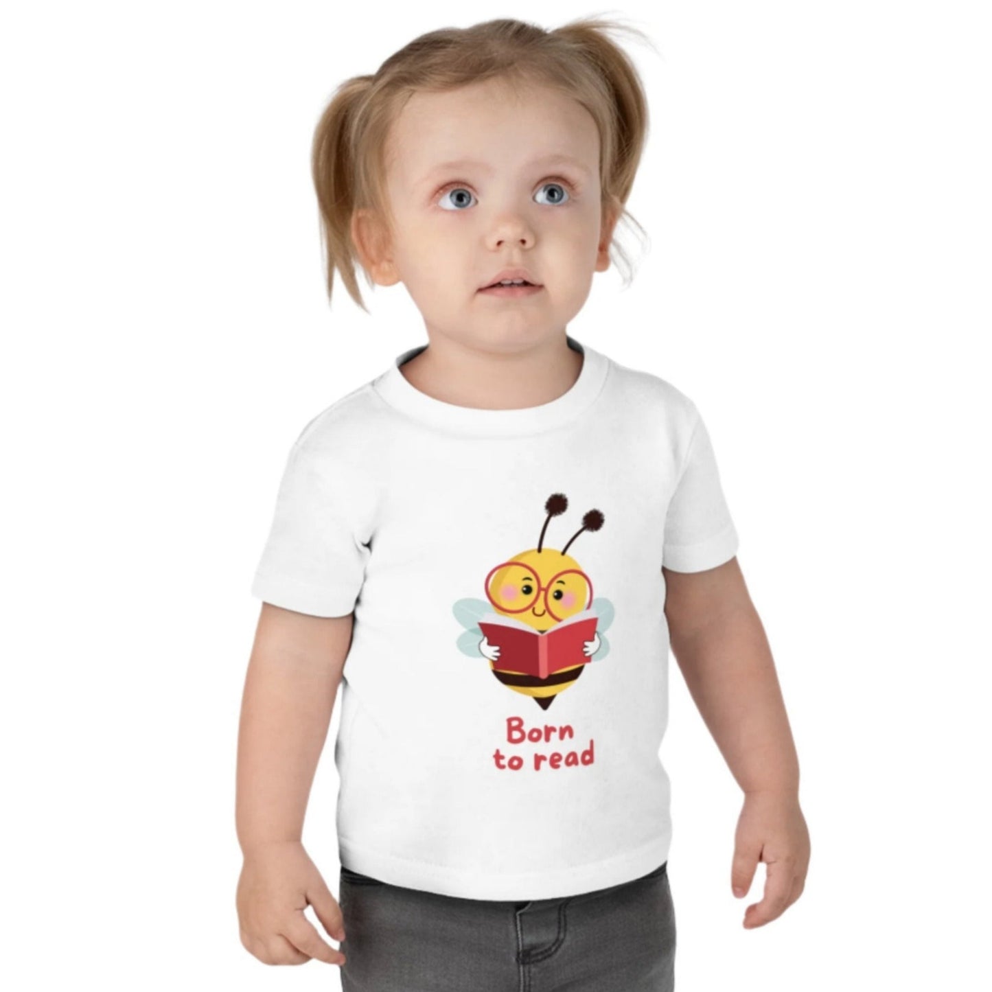 A toddler wearing a white t-shirt with a cartoon bee design and the phrase 'Bee a reader' printed on it.