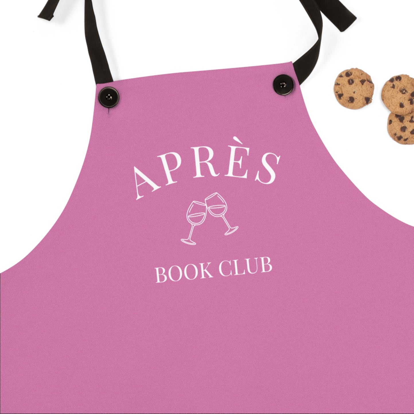 Pink apron with 'APRÈS BOOK CLUB' text and wine glass graphics on a white background.