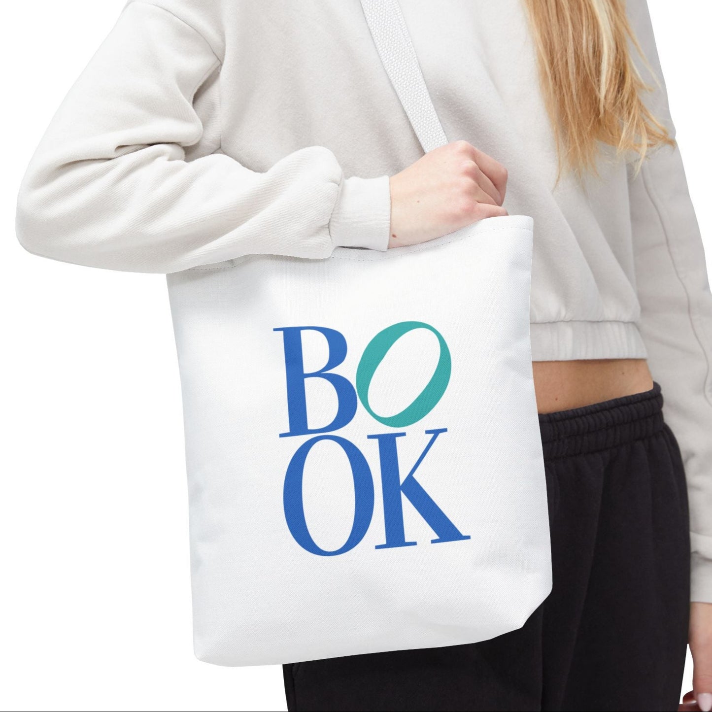 Person holding a white tote bag with 'BOOK' printed on it against a white background
