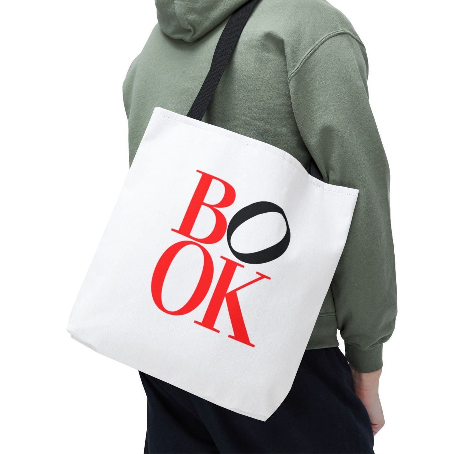 Man wearing a green hoodie carrying a white tote bag with 'BOOK' printed on it.