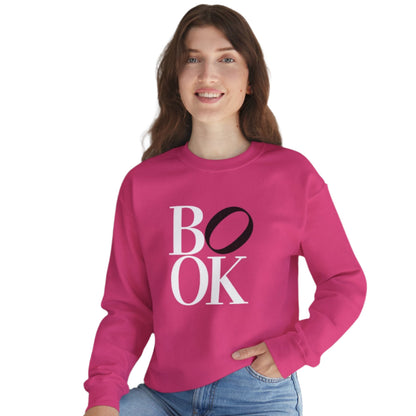 Person wearing a pink sweatshirt with 'BOOK' text, sitting indoors with a plant in the background