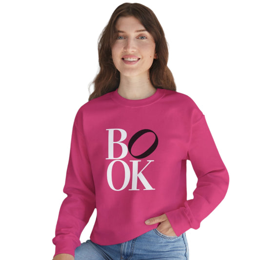 Person wearing a pink sweatshirt with 'BOOK' text, sitting indoors with a plant in the background