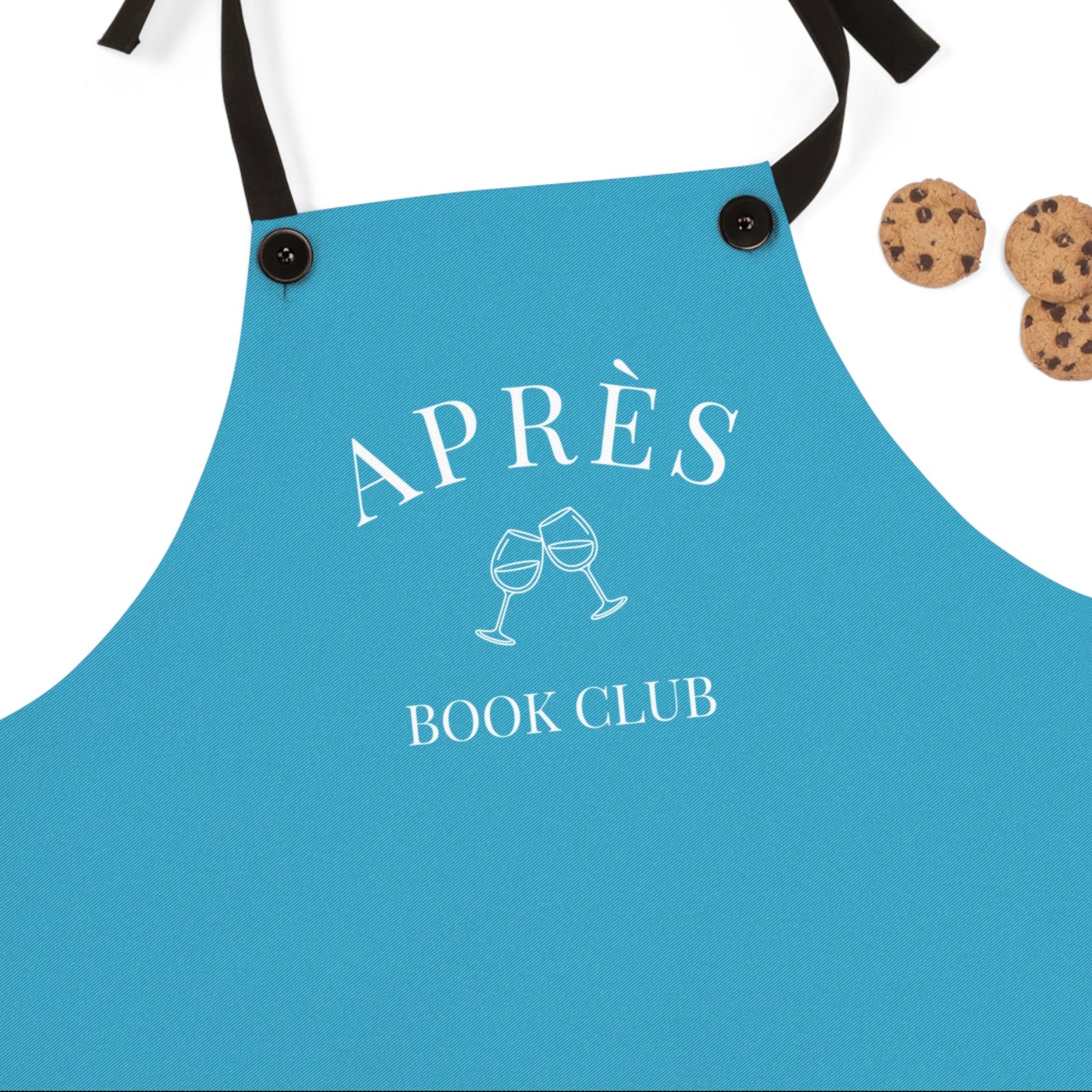 Blue apron with 'APRÈS BOOK CLUB' text and wine glass design, accompanied by cookies on a white background.