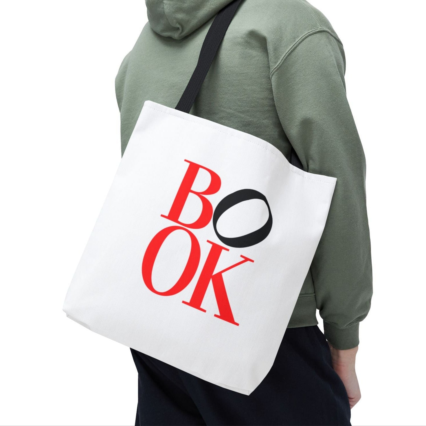 Man wearing a green hoodie carrying a white tote bag with 'BOOK' printed on it.