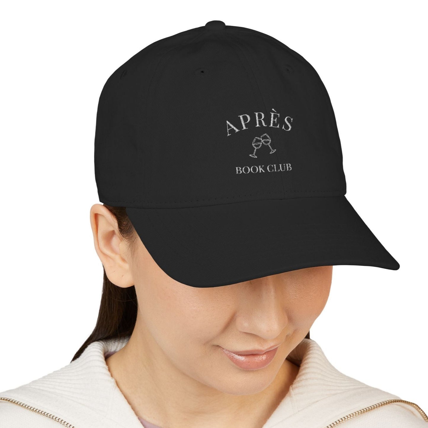 Black cap with 'APRèS BOOK CLUB' text worn by a person on a white background