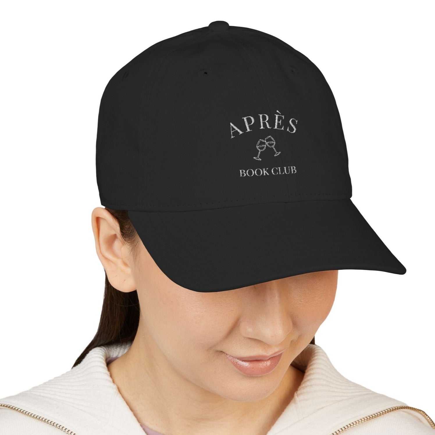 Black cap with 'APRèS BOOK CLUB' text worn by a person on a white background